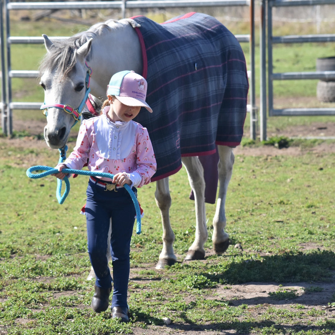 A 3 year old child leading her grey pony in a blue wooden rug to get ready for a riding lesson